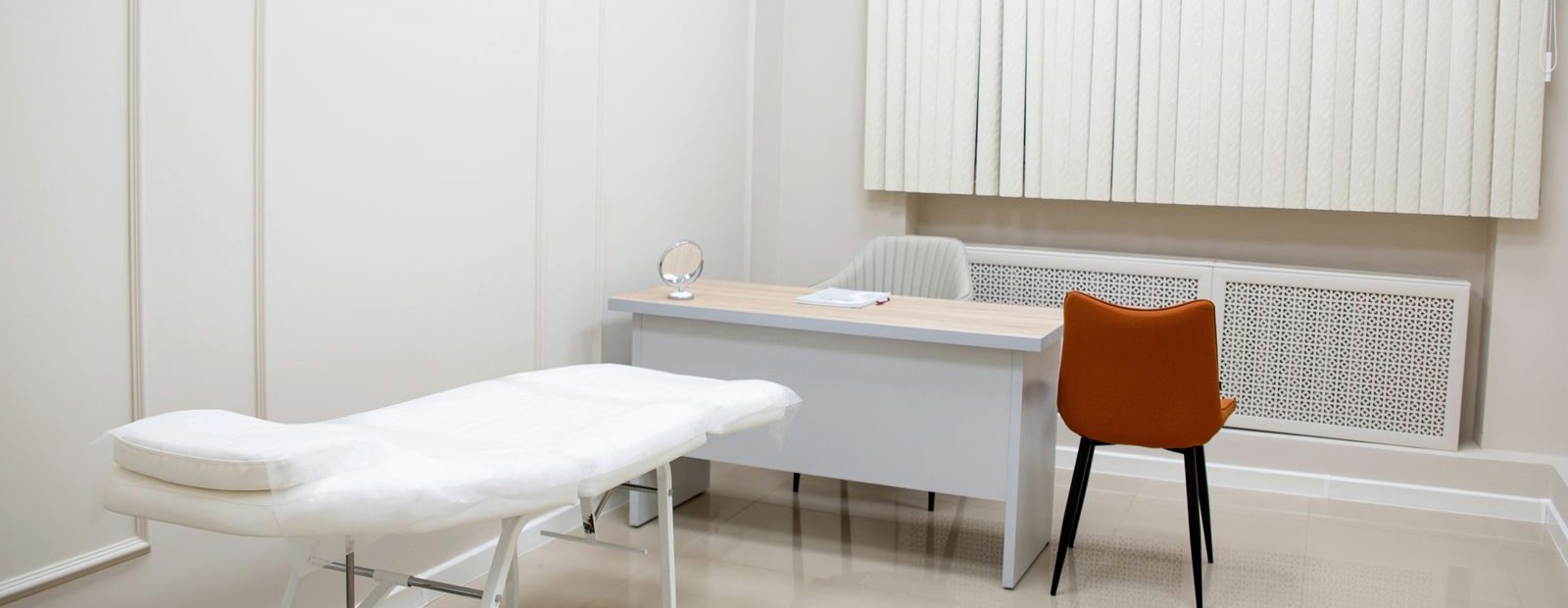 An empty, brightly lit clinical consultation room with an examination couch and desk