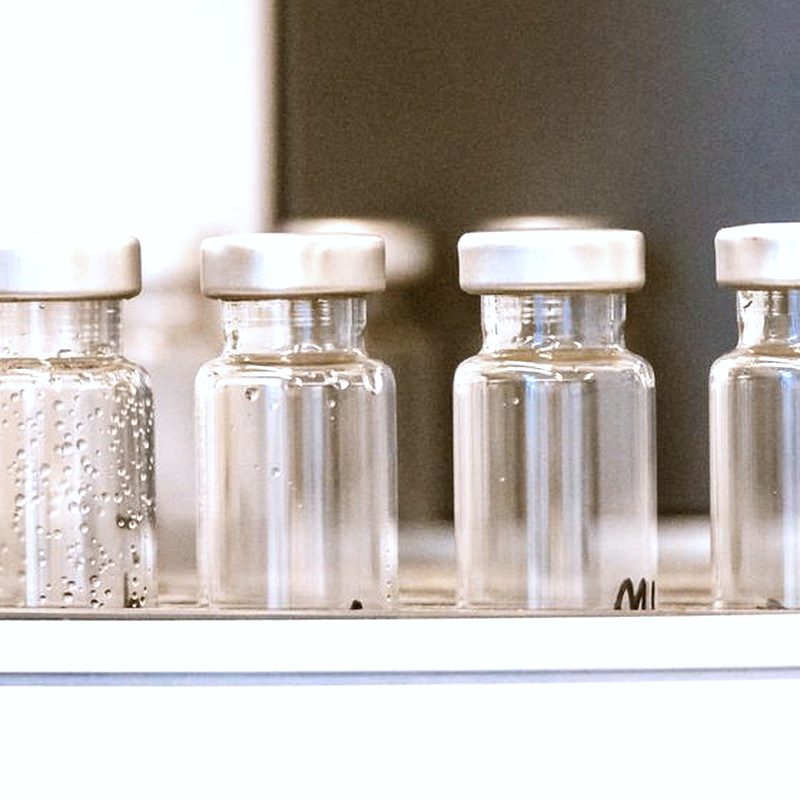 A row of clear sealed glass medical vials with aluminium crimp caps