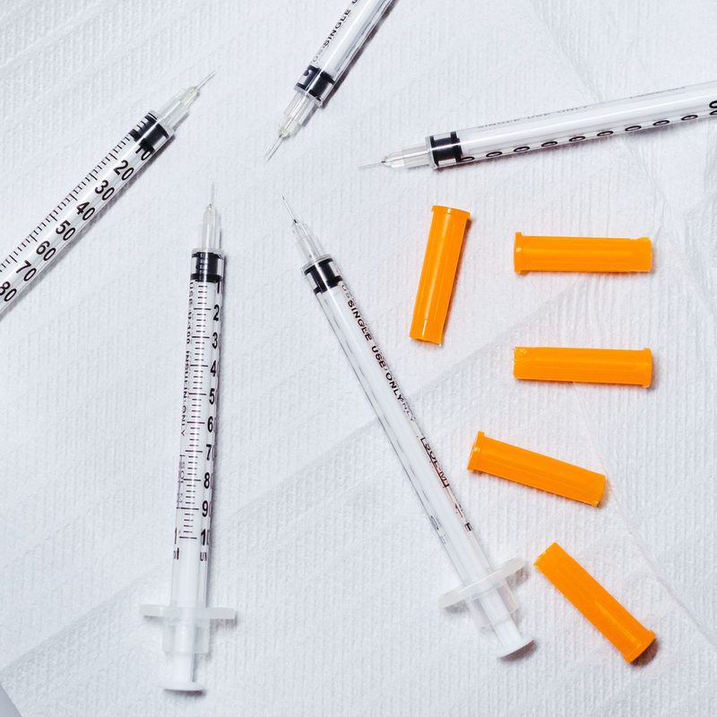 Single-use insulin-style syringes with orange needle caps on a white surface